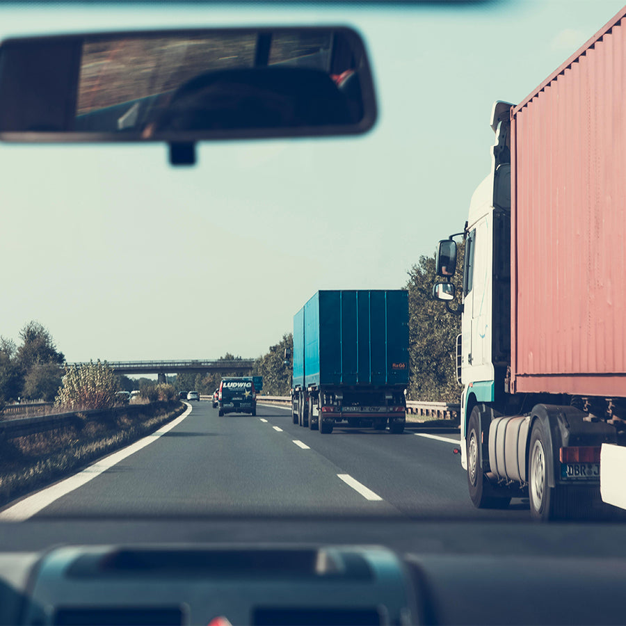 An image of 2 eighteen wheelers, on the road with the rearview mirror in a following vehicle.